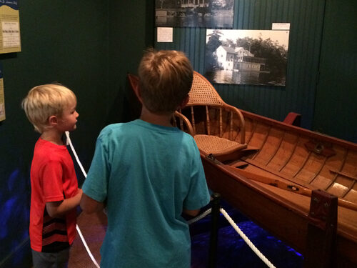 Two kids look at a boat in a museum gallery.